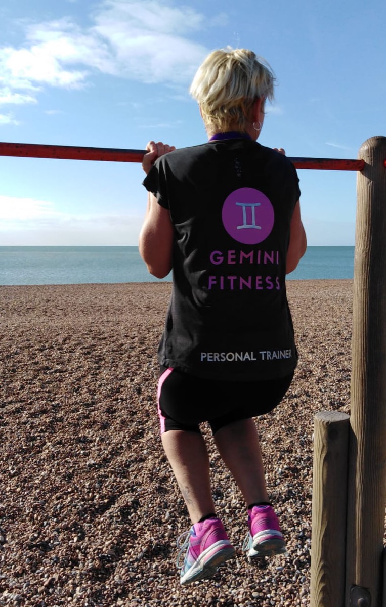 Lucie Collins on the shingle beach in a Gemini Fitness Personal Trainer top, pulling up on the red seafront rail